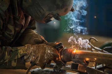 Welder at work. Man in a protective mask. The welder makes seams on the metal. Sparks and smoke...