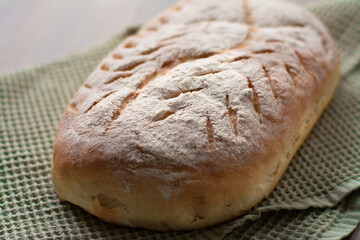 Homemade artisan sourdough bread loaf with artistic leaf pattern scoring and a wavy line in the middle on a green kitchen towel on wooden surface. Rustic aesthetic 