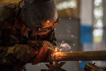 Welder at work. Man in a protective mask. The welder makes seams on the metal. Sparks and smoke...