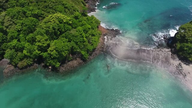 Overhead Strafe Flying Aerial View of Cavada Island Water Edge with Dense Jungle Trees and Rock Cliff Shore
