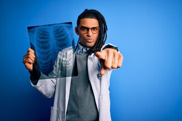 Young african american afro doctor man with dreadlocks holding chest lung xray pointing with finger to the camera and to you, hand sign, positive and confident gesture from the front