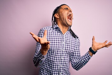 Fototapeta premium Young handsome african american afro man with dreadlocks wearing casual shirt celebrating mad and crazy for success with arms raised and closed eyes screaming excited. Winner concept