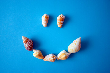 Happy emoji made of seashells on blue background. Summer, fun, vacation, travel, journey concept.