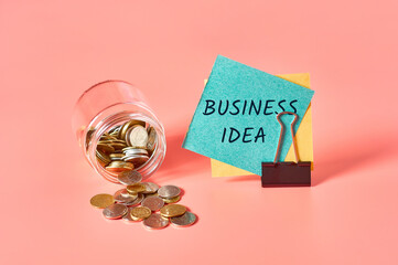 Glass jar with coins and paper sticker with inscription business idea on pink background