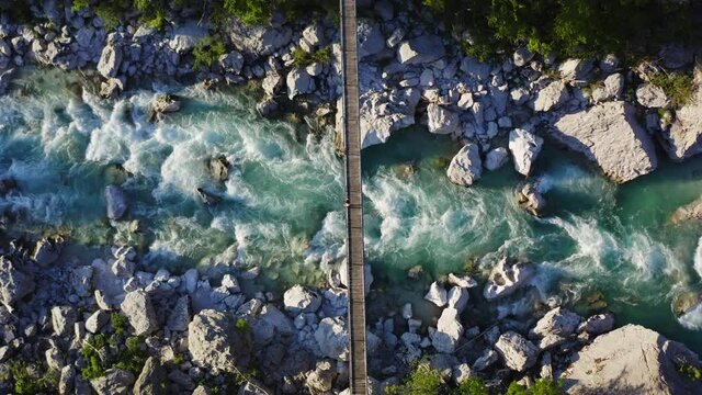 Aerial shot of a gril running, taking photos relaxing on a hanging bridge over emerald river Soca, Slovenia