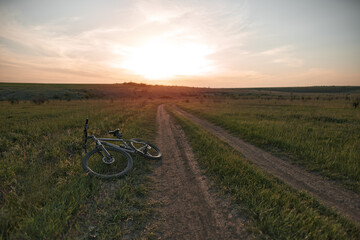 Fototapeta na wymiar Mountain bike lies on the ground during beautiful sunset on the horizon. Mountain bicycle