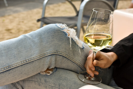 Elegant woman dressed in fashionable black shirt and jeans with glass of white wine, relaxing alcoholic drink.