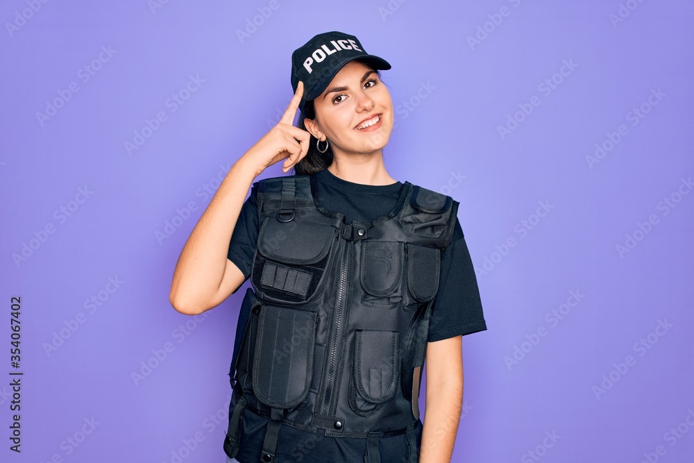 Sticker young police woman wearing security bulletproof vest uniform over purple background smiling pointing