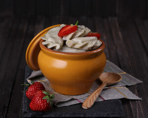 Russian and ukrainian cuisine. Dumplings with strawberry in a pot on an old wooden background. Boiled dough with filling. Spoon. Rustic. Background image, copy space