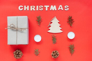 Christmas composition or ornament on red background from wooden inscription Christmas, cones, wooden Christmas tree, candles and branches of spruce. Copy space, space for text, flatly.