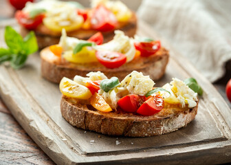 Tomato bruschetta and mozzarella cheese with basil on a rustic wooden board