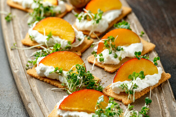 Cottage cheese and nectarine wedges on melba toast appetizers drizzled with runny honey and served with cress salad microgreen. Healthy party finger food