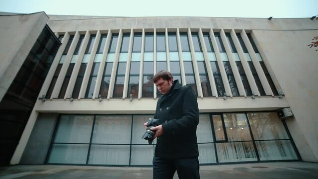 A photographer in a black coat standing on the street makes frames from the camera while shooting in different directions.