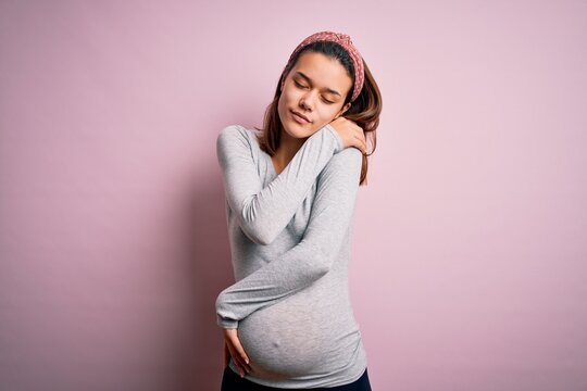 Young Beautiful Teenager Girl Pregnant Expecting Baby Over Isolated Pink Background Hugging Oneself Happy And Positive, Smiling Confident. Self Love And Self Care