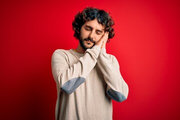 Fototapeta na wymiar Young handsome man with beard wearing casual sweater standing over red background sleeping tired dreaming and posing with hands together while smiling with closed eyes.