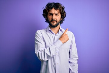 Young handsome business man with beard wearing shirt standing over purple background Pointing with hand finger to the side showing advertisement, serious and calm face