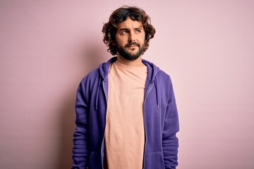 Young handsome sporty man with beard wearing casual sweatshirt over pink background smiling looking to the side and staring away thinking.