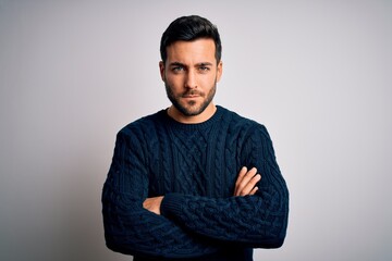 Young handsome man with beard wearing casual sweater standing over white background skeptic and...