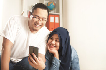 Asian muslim couple smiling happy when looking at smart phone, good news on internet