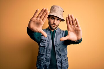Naklejka premium Handsome tourist man with beard on vacation wearing explorer hat over yellow background doing frame using hands palms and fingers, camera perspective