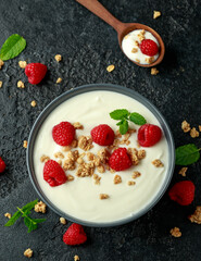 Greek yogurt with granola and raspberry in black bowl. Healthy breakfast food or snack