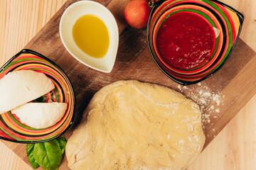 Stock photo of pizza dough on wooden board. Mozzarella, basil, tomato and oil around the dough