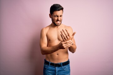 Young handsome strong man with beard shirtless standing over isolated pink background Suffering...