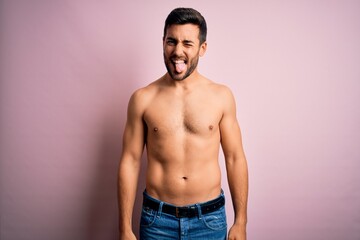 Young handsome strong man with beard shirtless standing over isolated pink background sticking tongue out happy with funny expression. Emotion concept.