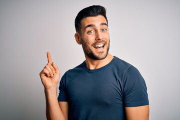 Young handsome man wearing casual t-shirt standing over isolated white background with a big smile on face, pointing with hand and finger to the side looking at the camera.