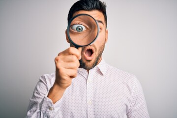 Young detective man looking through magnifying glass over isolated background scared in shock with a surprise face, afraid and excited with fear expression