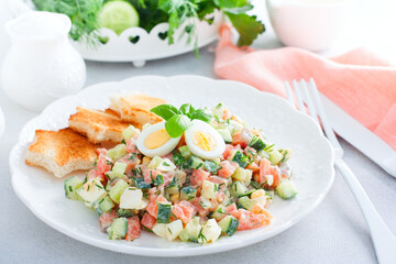 Salad with red fish, fresh cucumbers and herbs, an egg on a white plate with white bread toasts, selective focus