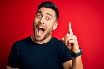 Young handsome man wearing casual black t-shirt standing over isolated red background pointing...