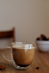 Glass cup with coffee and milk standing in the wooden table with chocolate candies and cinnamone 