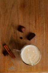 Glass cup with coffee and milk standing in the wooden table with chocolate candies and cinnamone 