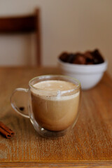Glass cup with coffee and milk standing in the wooden table with chocolate candies and cinnamone 