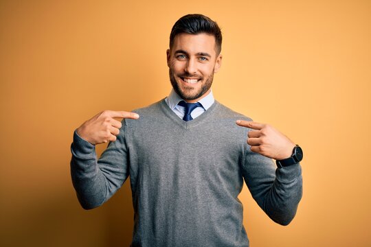 Young handsome businessman wearing elegant sweater and tie over yellow background looking confident with smile on face, pointing oneself with fingers proud and happy.