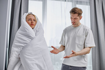 Fototapeta premium How much can you sleep young man dissatisfied with lazy wife, woman stand wrapped in a blanket