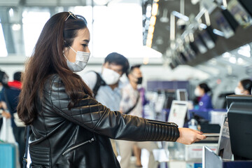 Asian female traveler wearing mask give passport to check in counter.