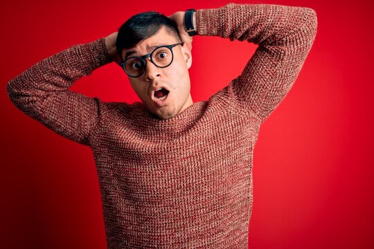 Young handsome hispanic man wearing nerd glasses over red background Crazy and scared with hands on head, afraid and surprised of shock with open mouth