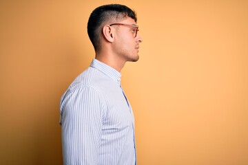 Young handsome hispanic business man wearing nerd glasses over yellow background looking to side,...