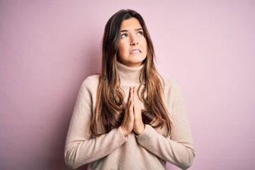 Young beautiful girl wearing casual turtleneck sweater standing over isolated pink background begging and praying with hands together with hope expression on face very emotional and worried. Begging.