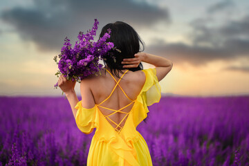 Summer mood. A woman in a luxurious yellow dress is standing in a purple flowering field with her back to the camera. Close up.
