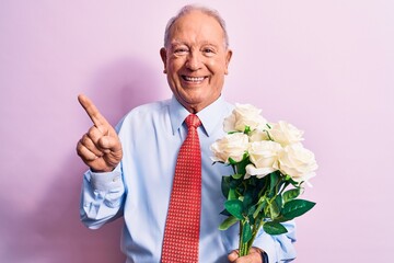 Senior grey-haired businessman wearing tie holding bouquet of flowers over pink background smiling happy pointing with hand and finger to the side