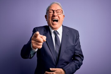 Grey haired senior business man wearing glasses and elegant suit and tie over purple background...