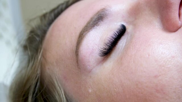 Close up eyelash extension Procedure. Eyelash extension master glues long artificial eyelashes to the woman client in beauty salon. 4k footage. 
