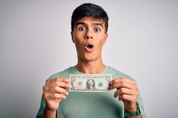 Young handsome man holding one dollar banknotes over isolated white background scared in shock with a surprise face, afraid and excited with fear expression