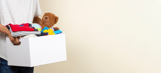Donation concept. Kid hands holding donate box with books, clothes and toys