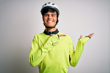 Young handsome cyclist man wearing security bike helmet over isolated white background amazed and smiling to the camera while presenting with hand and pointing with finger.