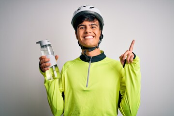 Young handsome cyclist man wearing security bike helmet drinking bottle of water surprised with an idea or question pointing finger with happy face, number one