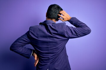 Young handsome business man wearing jacket and glasses over isolated purple background Backwards thinking about doubt with hand on head